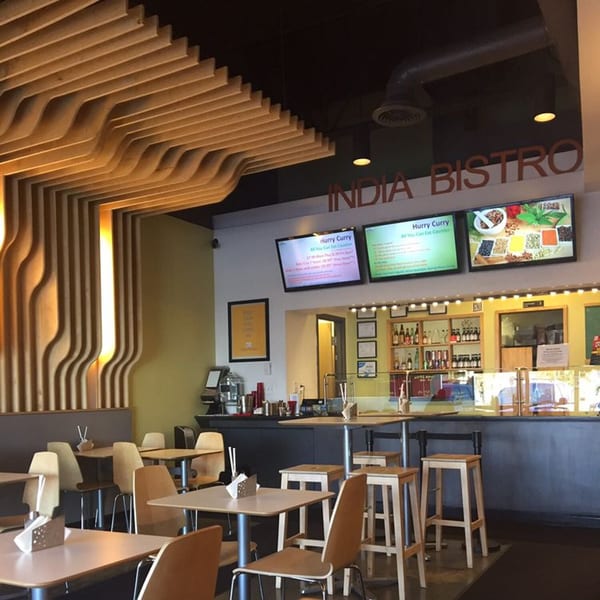 Interior of India Bistro with modern wooden ceiling, dining tables, and a counter with digital menus.